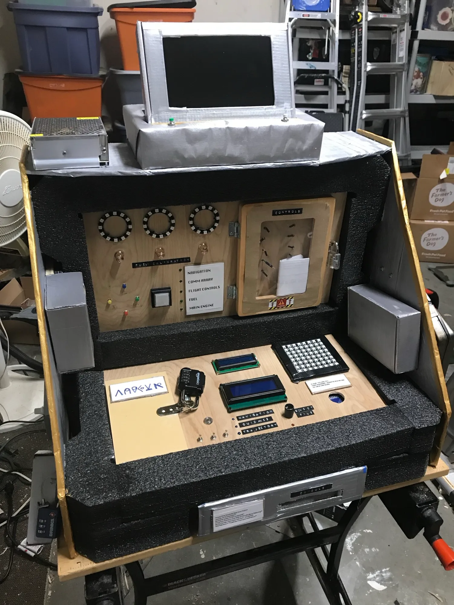 The complete portable escape room set up, foam and cardboard panels with the seven game stations mounted and the Pi monitor at the centre